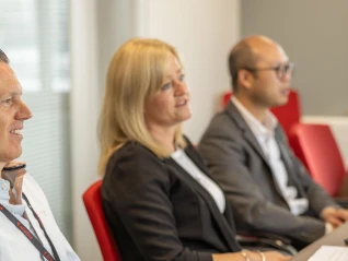 Two women and men in a large meeting room